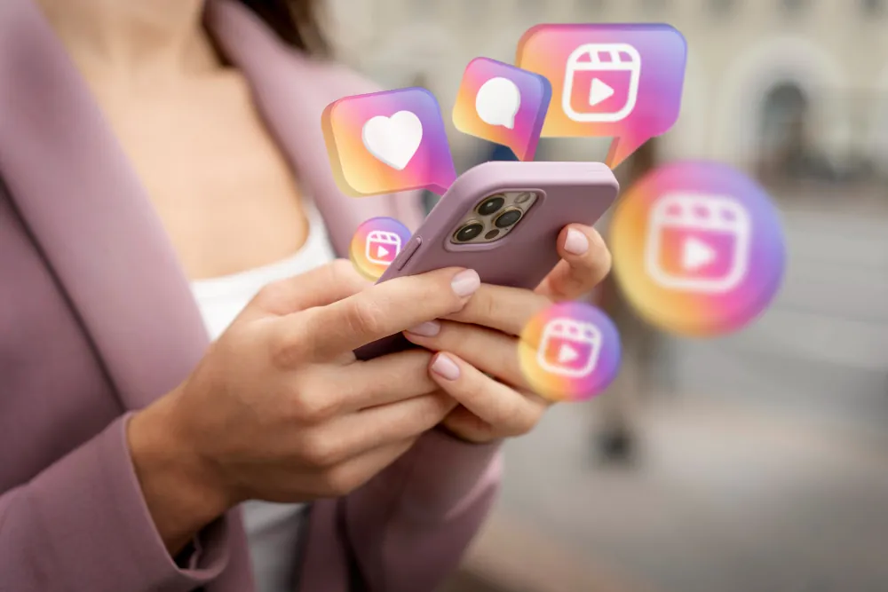 Mãos femininas segurando smartphone com ícones do Instagram Reels, curtidas e comentários, indicando interação em redes sociais.