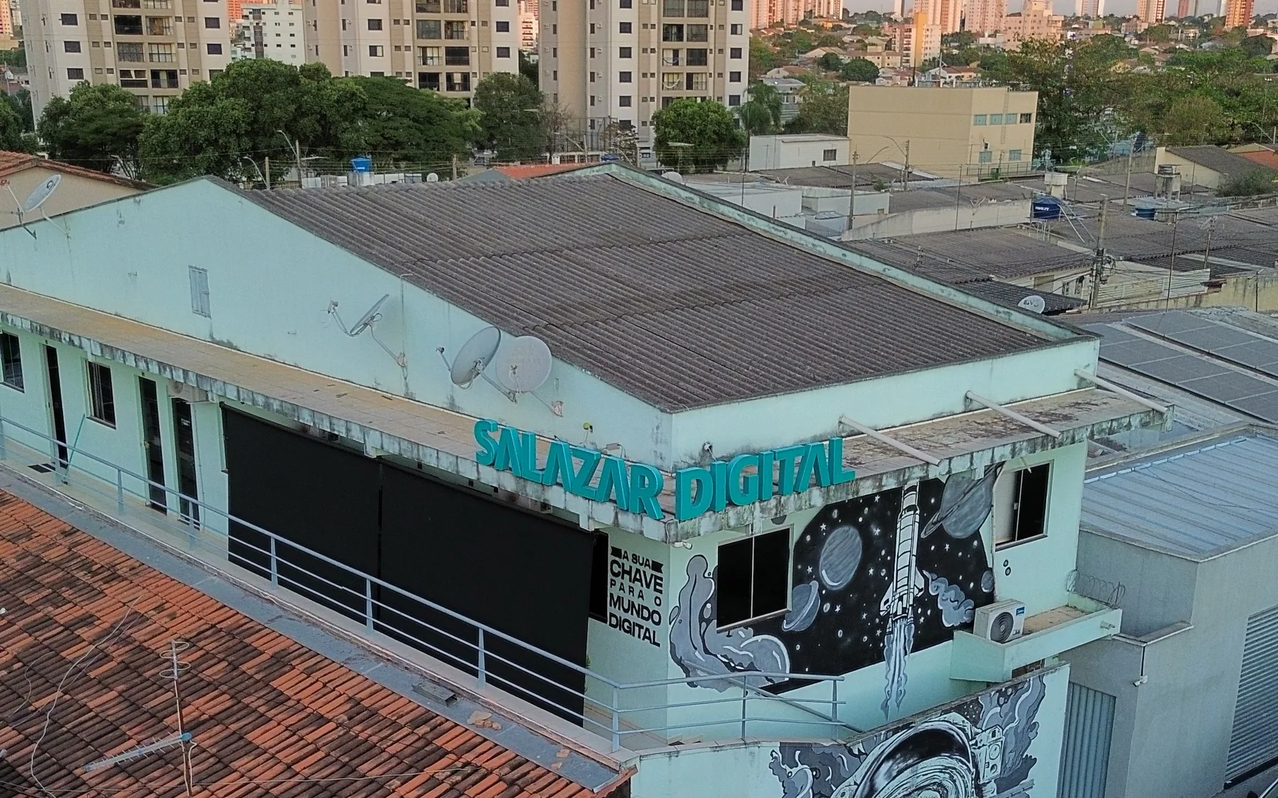 Vista aérea da sede da Salazar Digital em Goiânia, com o mural pintado na fachada e o skyline ao fundo.